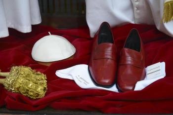 Detalle de unos zapatos de piel rojos y un solideo blanco expuestos en el escaparate de la sastrería italiana Gammarelli junto a varias sotanas (no aparecen) para el futuro papa.